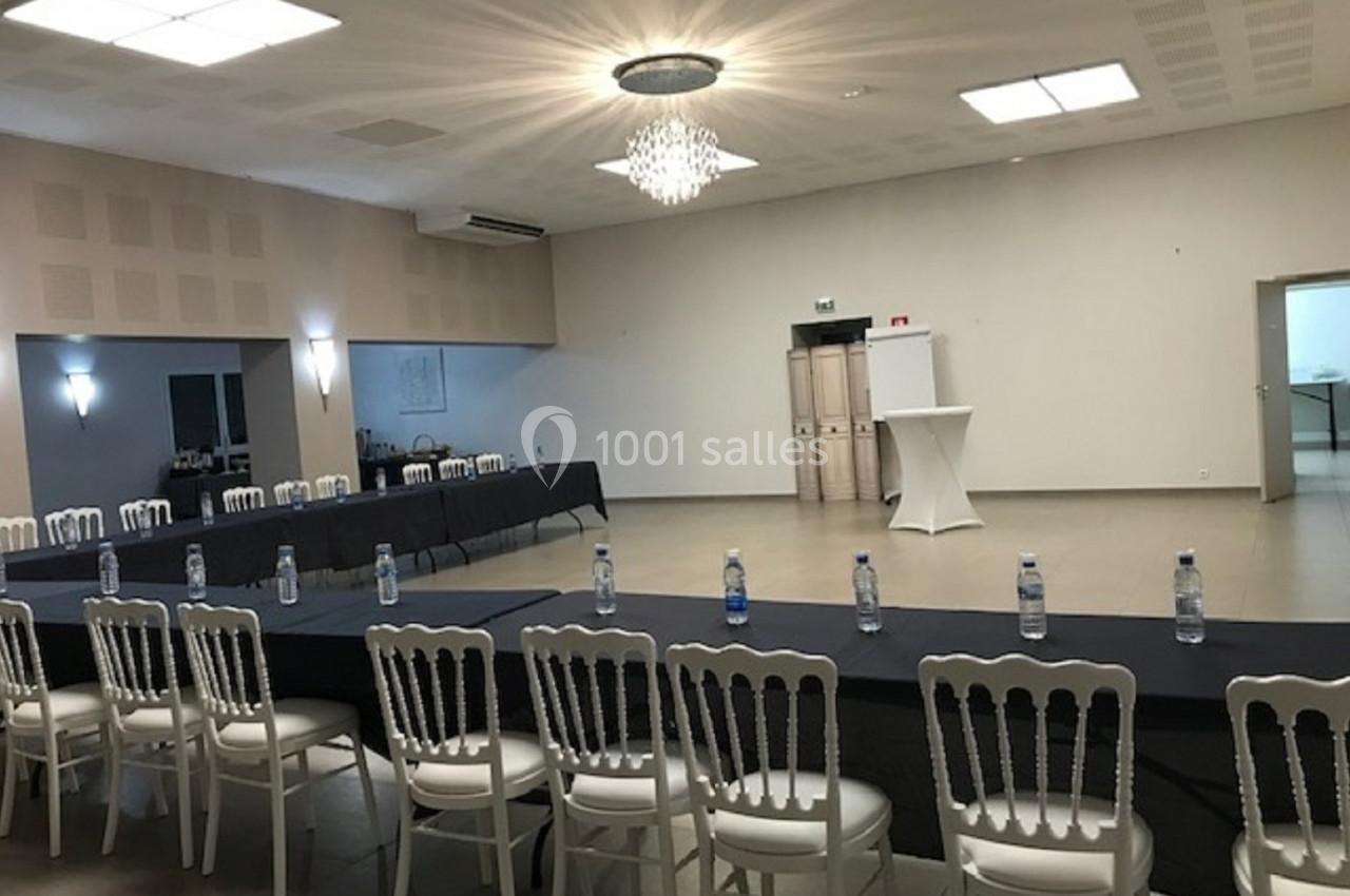 Salle de réunion lumineuse avec des tables disposées en U, des chaises blanches et des bouteilles d'eau alignées.