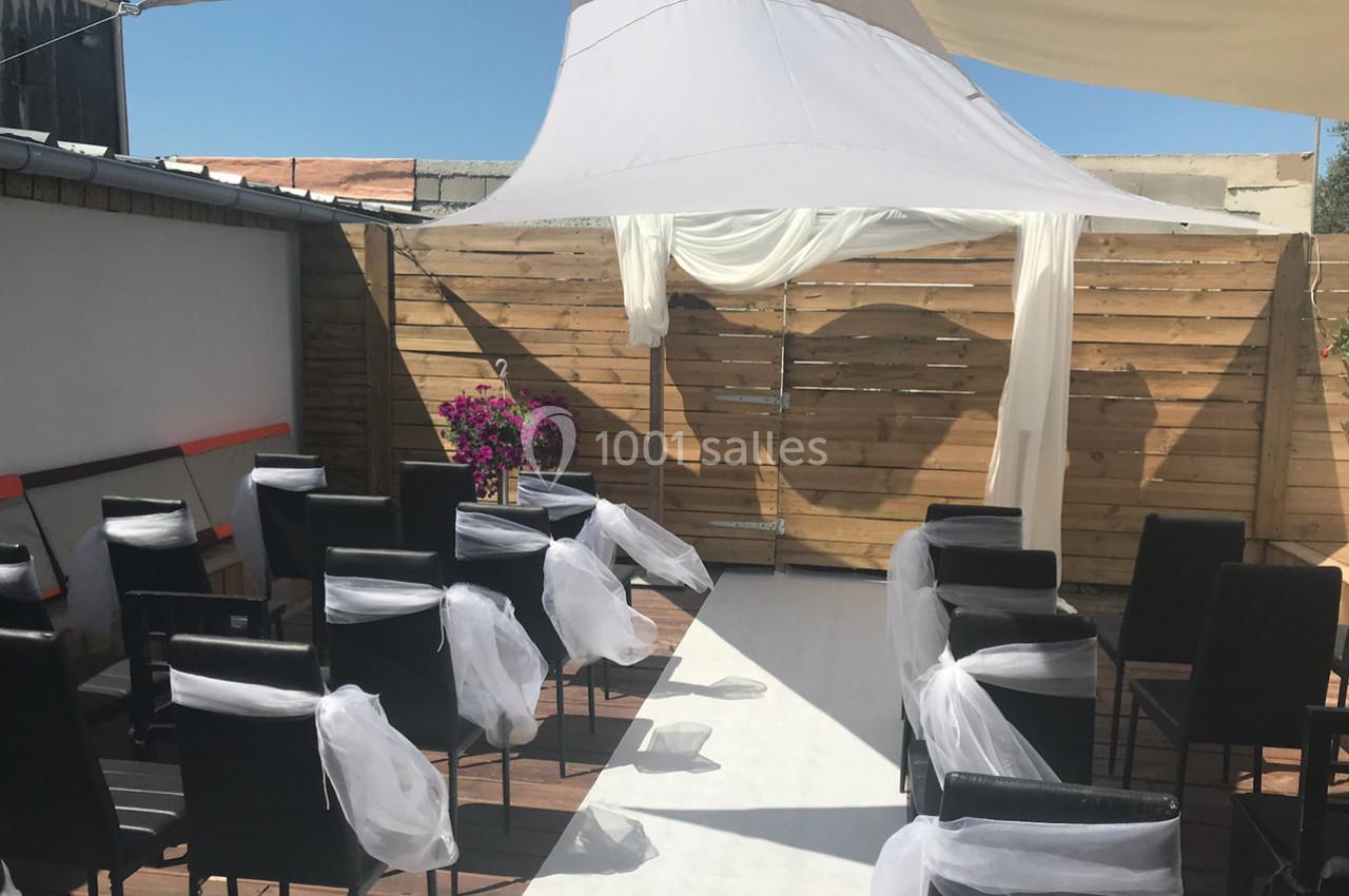 Chaises noires décorées de voiles blancs disposées devant une arche en bois sous une tente blanche en extérieur.