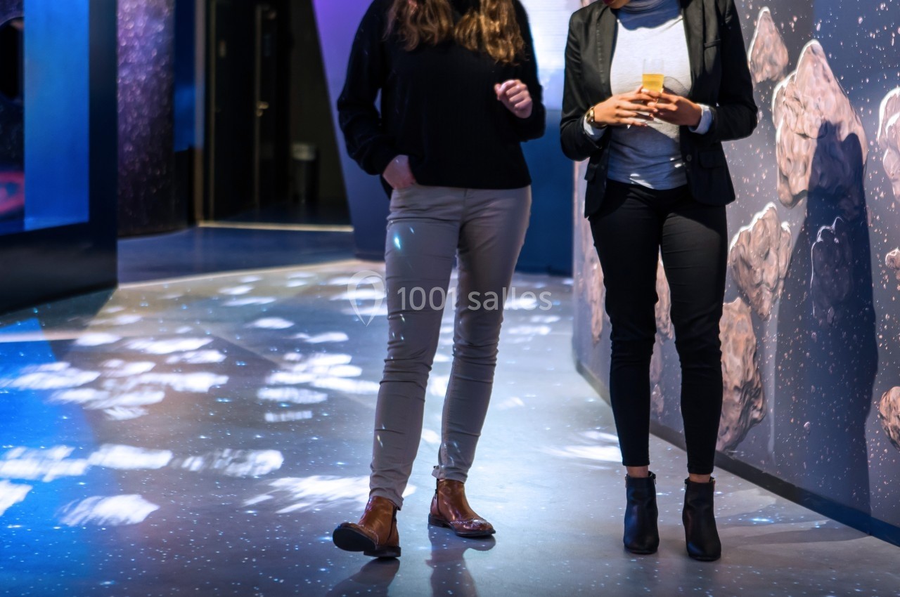 Deux personnes debout dans un espace d'exposition interactif, entourées de projections lumineuses au sol.