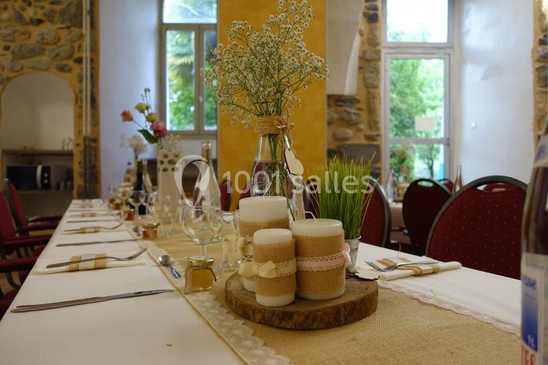 Table décorée pour un événement, avec bougies, fleurs et éléments rustiques, dans une salle lumineuse aux murs en pierre.