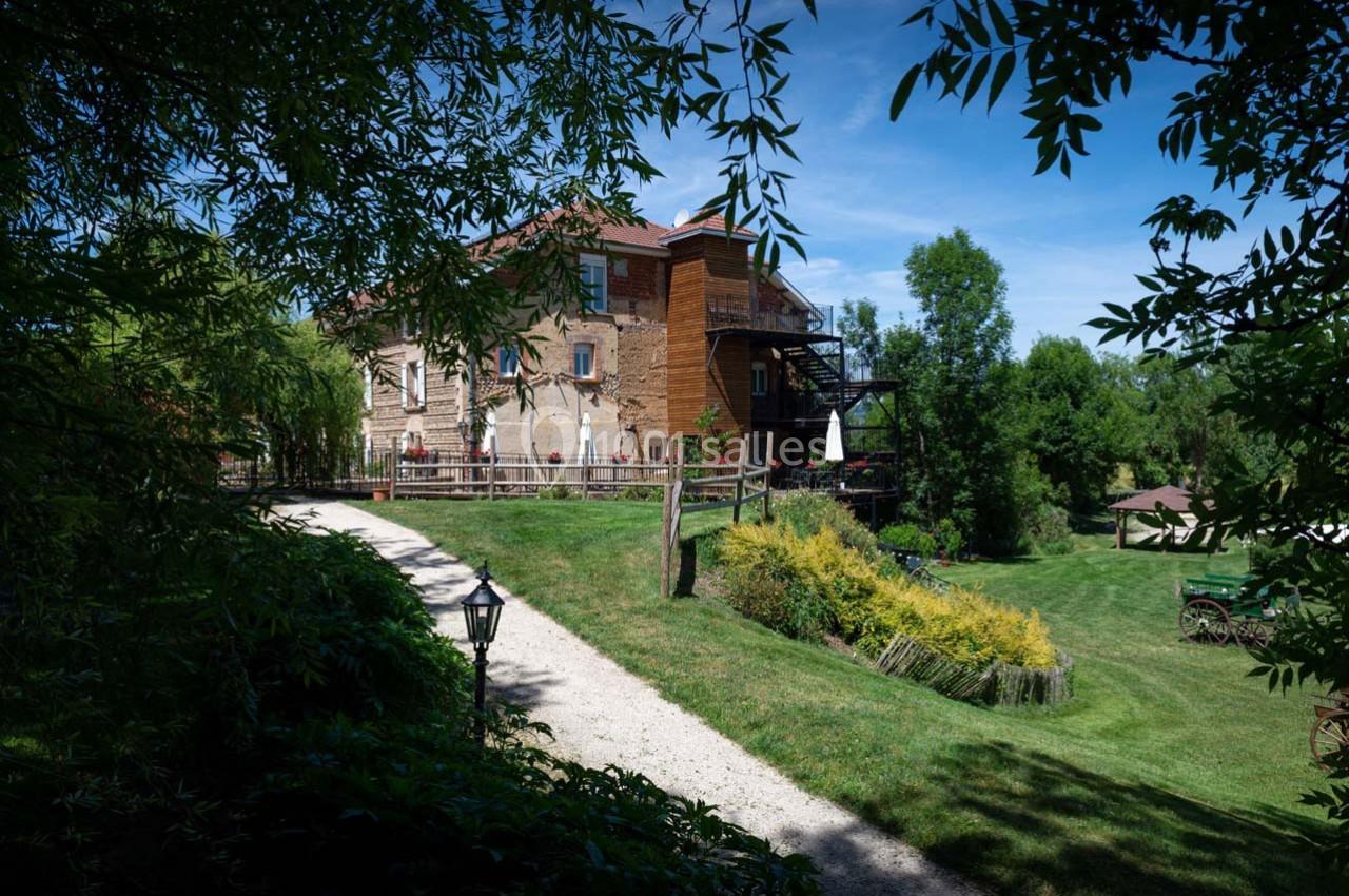 Chemin de gravier menant à une grande maison en briques entourée de verdure et d'arbres sous un ciel bleu.
