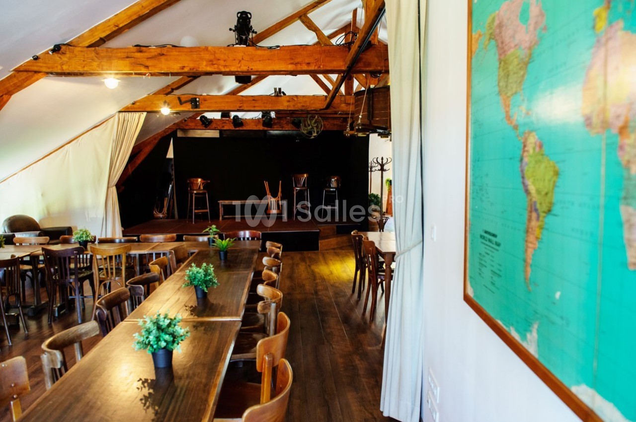 Salle avec des tables en bois, des chaises, une scène au fond et une carte du monde accrochée au mur.