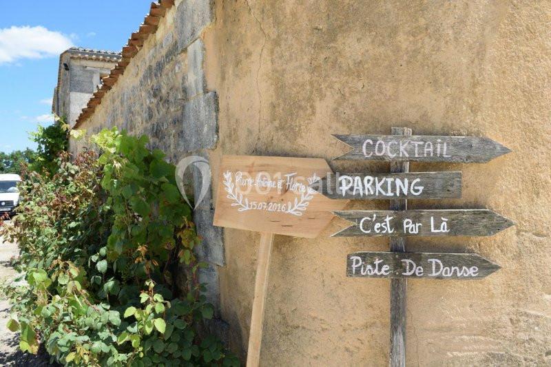 Panneaux en bois indiquant les directions pour un cocktail, un parking et une piste de danse près d'un mur en pierre.