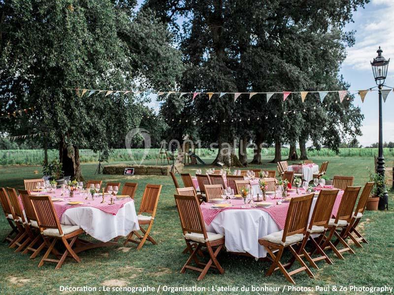 Tables décorées avec nappes rouges et blanches installées en extérieur sous des arbres, avec fanions suspendus.