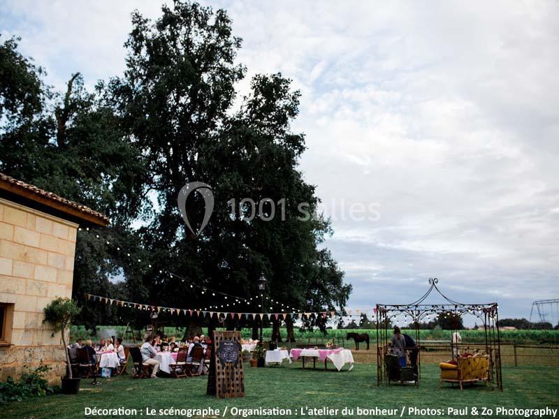 Réception en plein air avec tables dressées, guirlandes suspendues et invités dans un cadre champêtre.