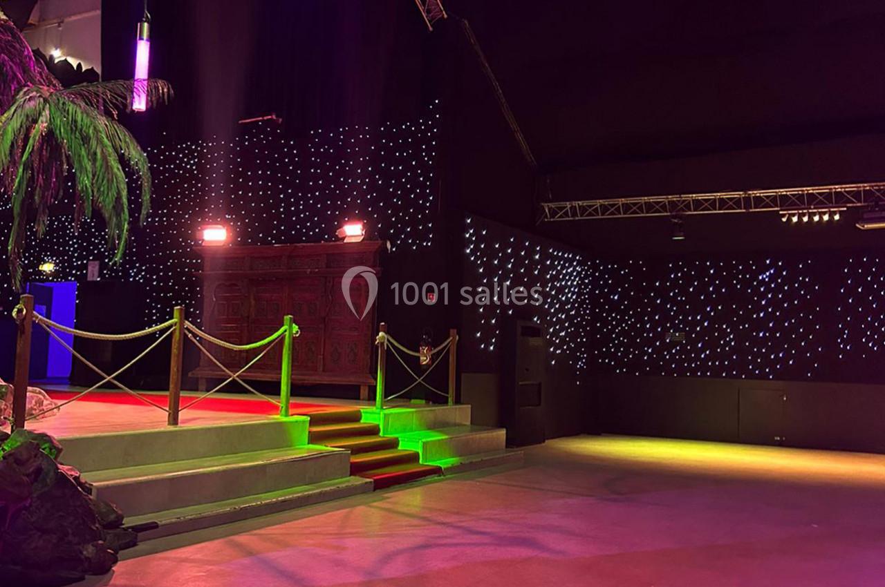 Scène illuminée avec des marches rouges, une rambarde dorée et un fond étoilé dans une salle sombre.