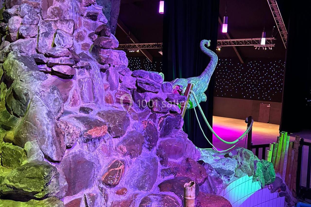 Rochers éclairés de lumières colorées avec une sculpture de dinosaure et une scène illuminée en arrière-plan.