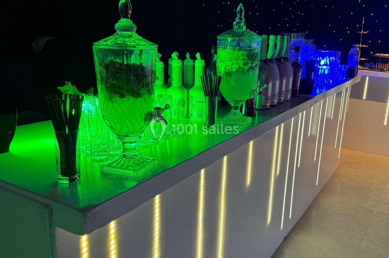 Bar éclairé avec des LED colorées, contenant des jarres de boissons, des verres et des accessoires de service.