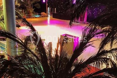 Décor intérieur avec éclairage coloré, fontaines illuminées, végétation tropicale et tables dressées en arrière-plan.