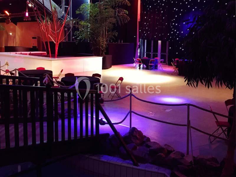 Salle aménagée avec des chaises dispersées, éclairage tamisé et décorations végétales sous un plafond étoilé.