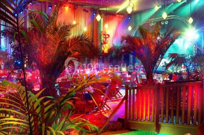 Décor intérieur avec éclairage coloré, fontaines illuminées, végétation tropicale et tables dressées en arrière-plan.