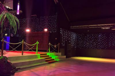 Décor intérieur avec éclairage coloré, fontaines illuminées, végétation tropicale et tables dressées en arrière-plan.