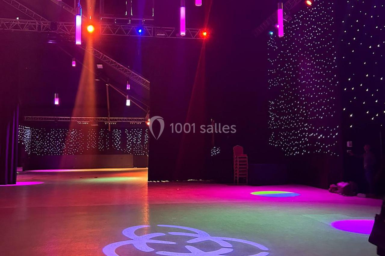 Salle sombre avec éclairages colorés suspendus, sol éclairé par des motifs lumineux et murs ornés de lumières étoilées.