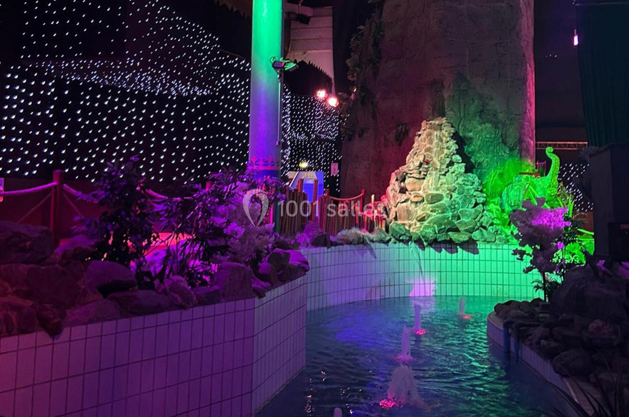 Piscine décorative éclairée par des lumières colorées, entourée de plantes, d'un rocher artificiel et d'une cascade.