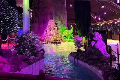 Décor intérieur avec éclairage coloré, fontaines illuminées, végétation tropicale et tables dressées en arrière-plan.
