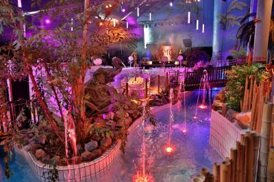 Décor intérieur avec éclairage coloré, fontaines illuminées, végétation tropicale et tables dressées en arrière-plan.