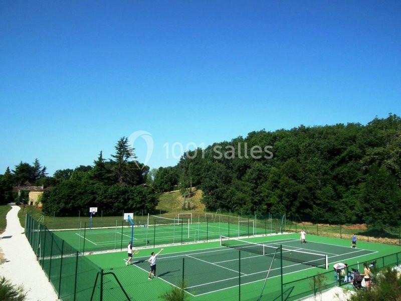 Terrains de tennis extérieurs entourés de verdure, avec des joueurs en action sous un ciel dégagé.