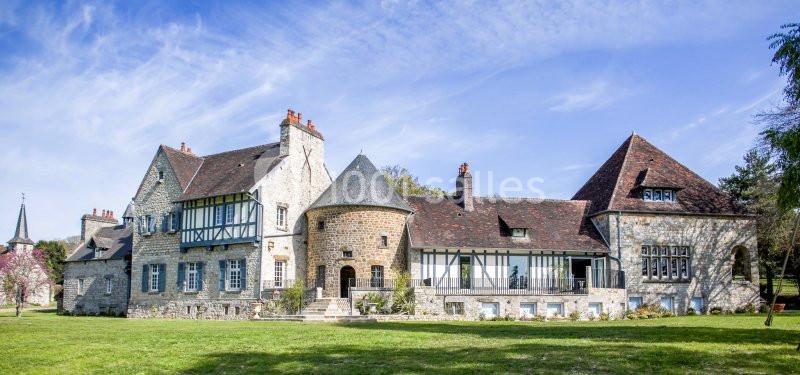 Grande maison en pierre avec toit en tuiles, entourée de verdure, sous un ciel bleu dégagé.