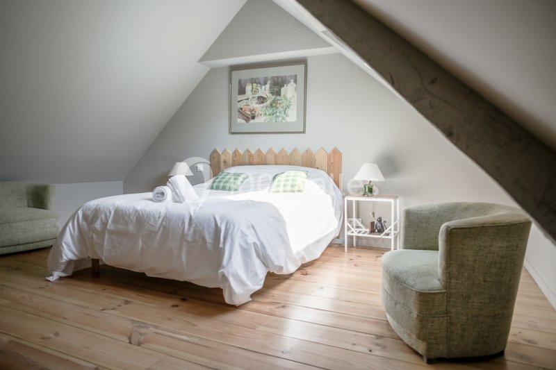 Chambre mansardée avec lit double, parquet en bois clair, fauteuil, table de chevet et décoration murale.