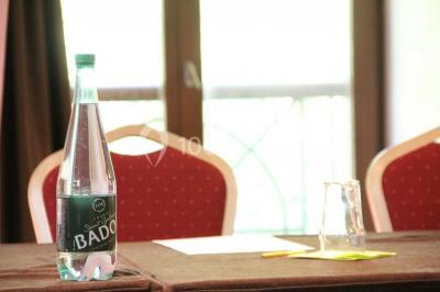 Vue nocturne d'une maison en bois éclairée, entourée d'arbres illuminés, sous un ciel nuageux avec la lune visible.