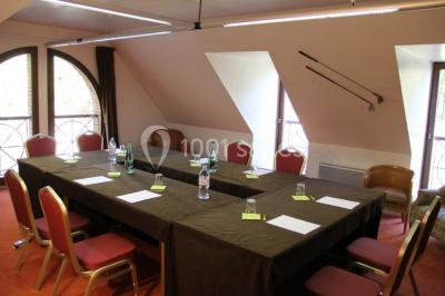 Vue nocturne d'une maison en bois éclairée, entourée d'arbres illuminés, sous un ciel nuageux avec la lune visible.