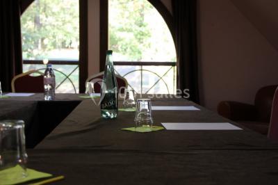 Vue nocturne d'une maison en bois éclairée, entourée d'arbres illuminés, sous un ciel nuageux avec la lune visible.