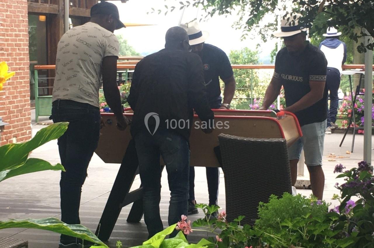 Quatre hommes jouent à un baby-foot en extérieur sur une terrasse entourée de plantes et de fleurs.