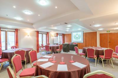 Vue nocturne d'une maison en bois éclairée, entourée d'arbres illuminés, sous un ciel nuageux avec la lune visible.