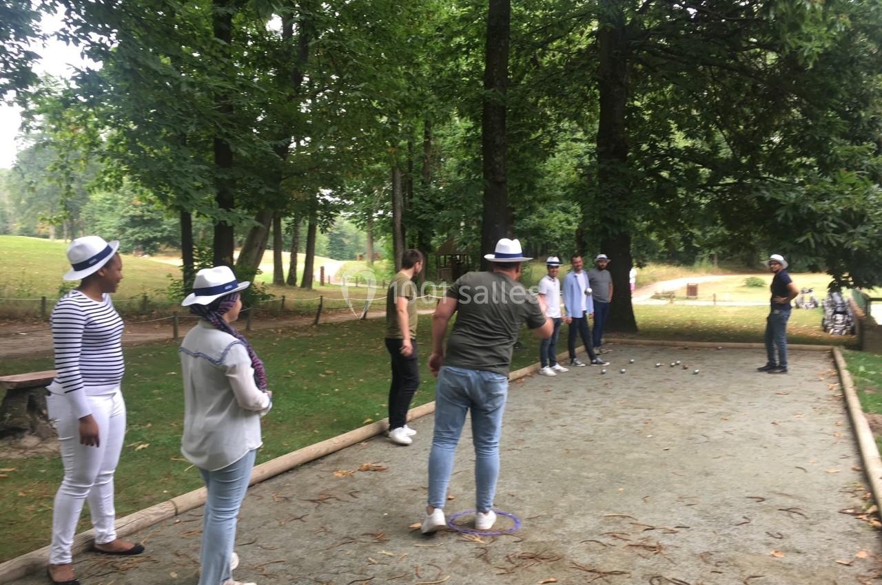 Des personnes jouent à la pétanque sur un terrain en plein air entouré d'arbres dans un parc.