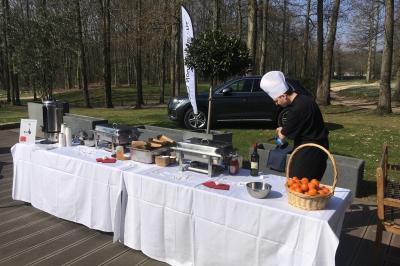 Vue nocturne d'une maison en bois éclairée, entourée d'arbres illuminés, sous un ciel nuageux avec la lune visible.