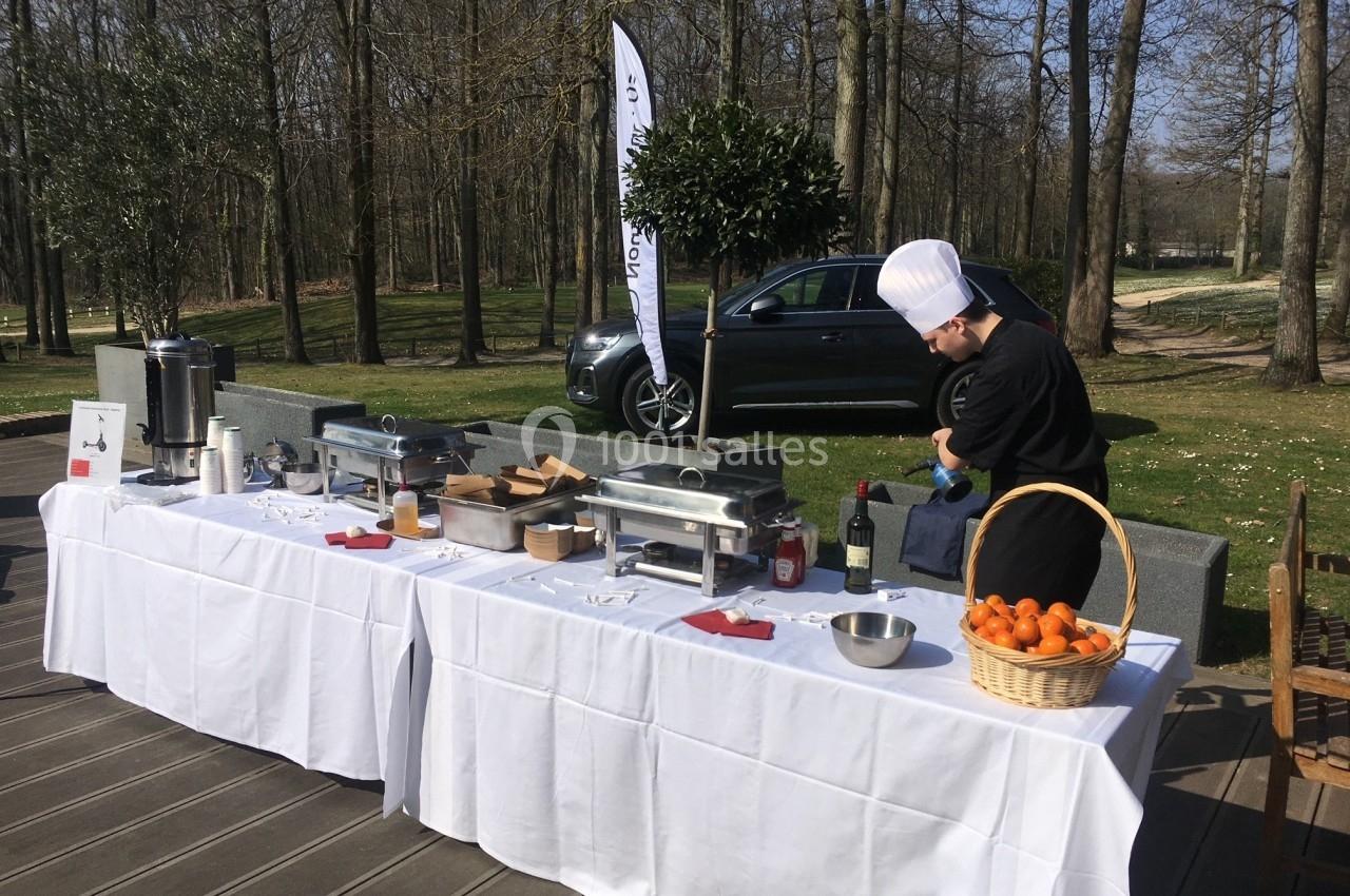 Un chef prépare une table de buffet en plein air avec des équipements de cuisine et un panier d'oranges.