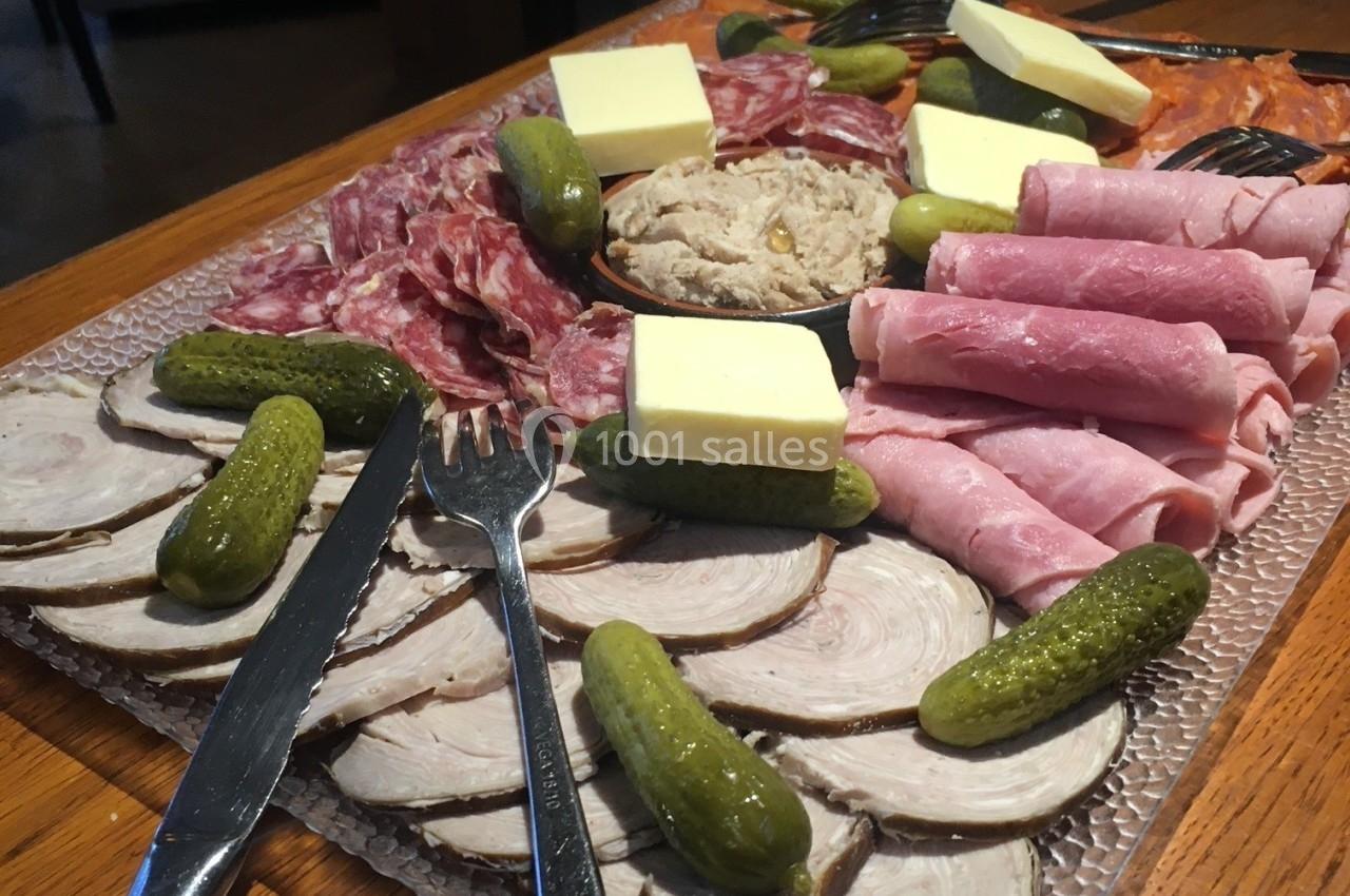 Plateau de charcuterie variée avec cornichons, beurre, pâté et tranches de jambon et saucisson sur une table en bois.