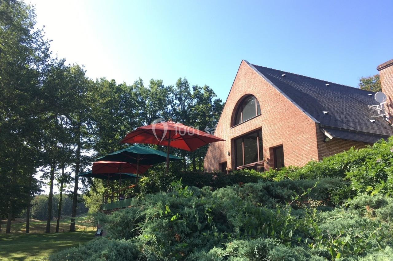 Maison en briques avec toit en ardoise, entourée de verdure, avec des parasols colorés sur une terrasse.
