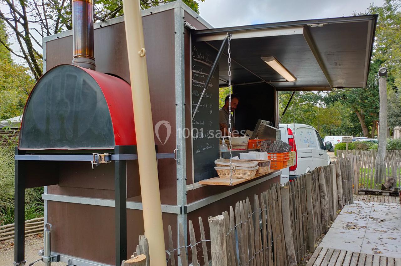 Four à bois mobile dans une remorque aménagée, entourée d'une clôture en bois, avec un cuisinier à l'intérieur.
