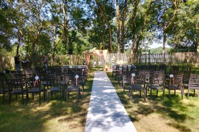 Espace extérieur décoré avec arche florale, deux chaises transparentes et fond blanc sous une tente.