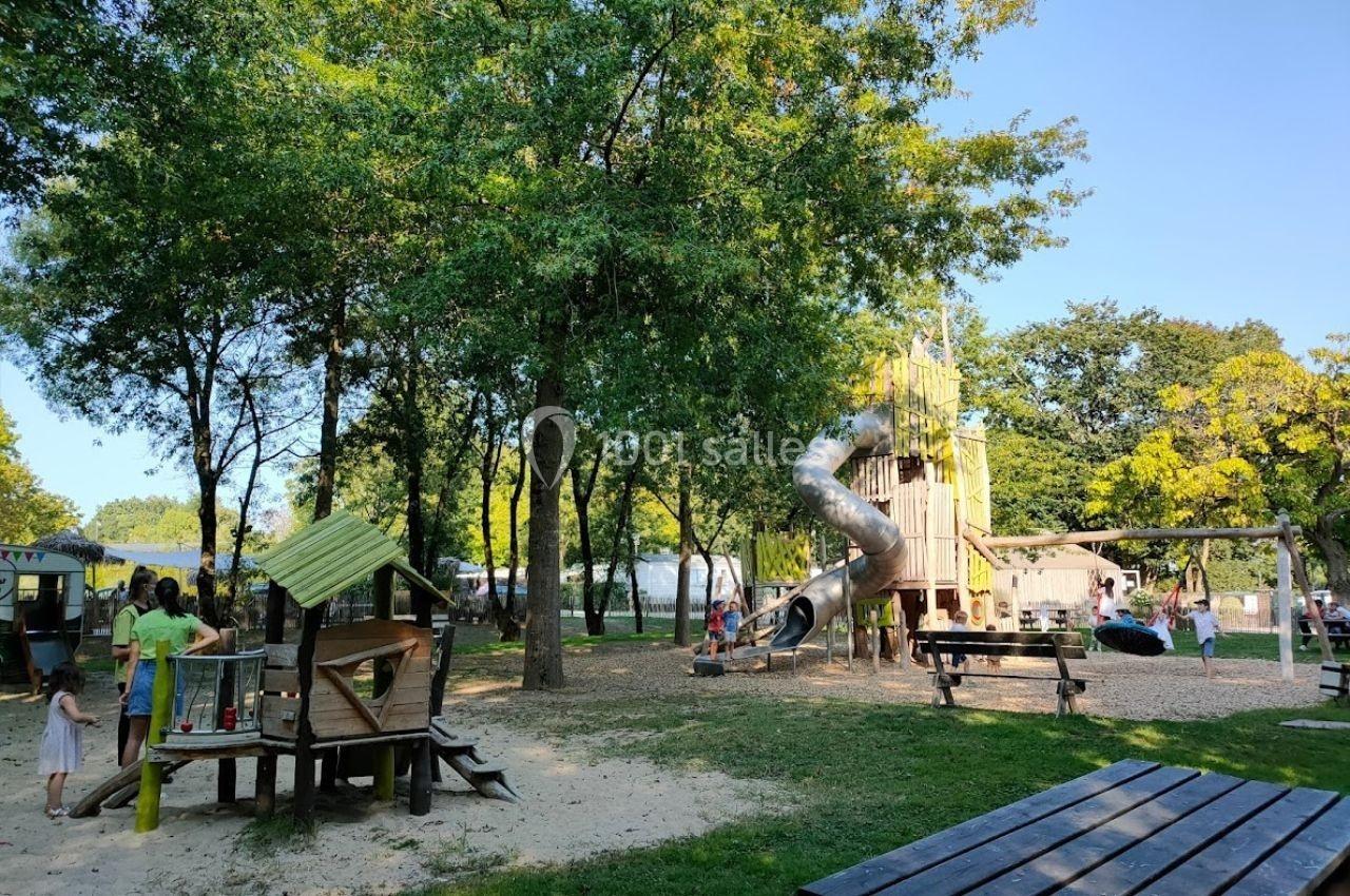 Aire de jeux en plein air avec toboggan, structures en bois, arbres et familles profitant de l'espace.