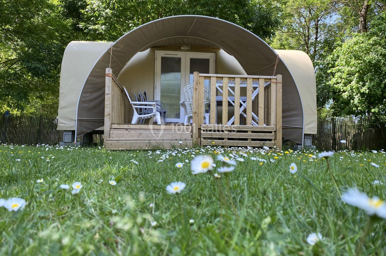 Hébergement en toile et bois avec terrasse, entouré de verdure et de fleurs blanches dans un cadre naturel.