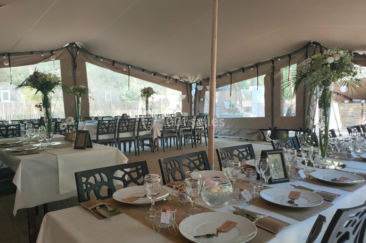 Salle de réception sous une tente avec tables décorées de nappes blanches, vaisselle élégante et arrangements floraux.