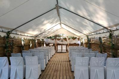 Espace extérieur décoré avec arche florale, deux chaises transparentes et fond blanc sous une tente.