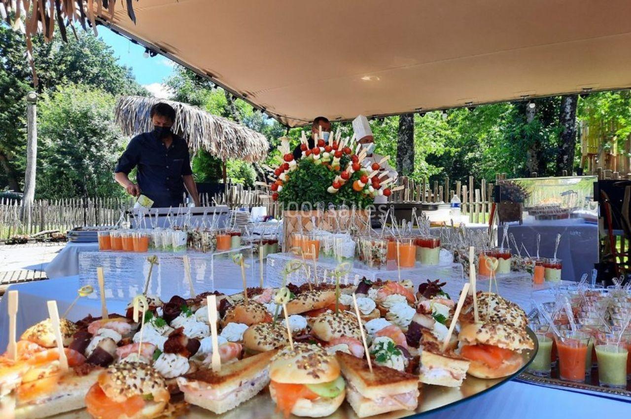 Buffet en plein air avec assortiments de canapés, verrines et brochettes, décoré de fleurs et entouré de verdure.