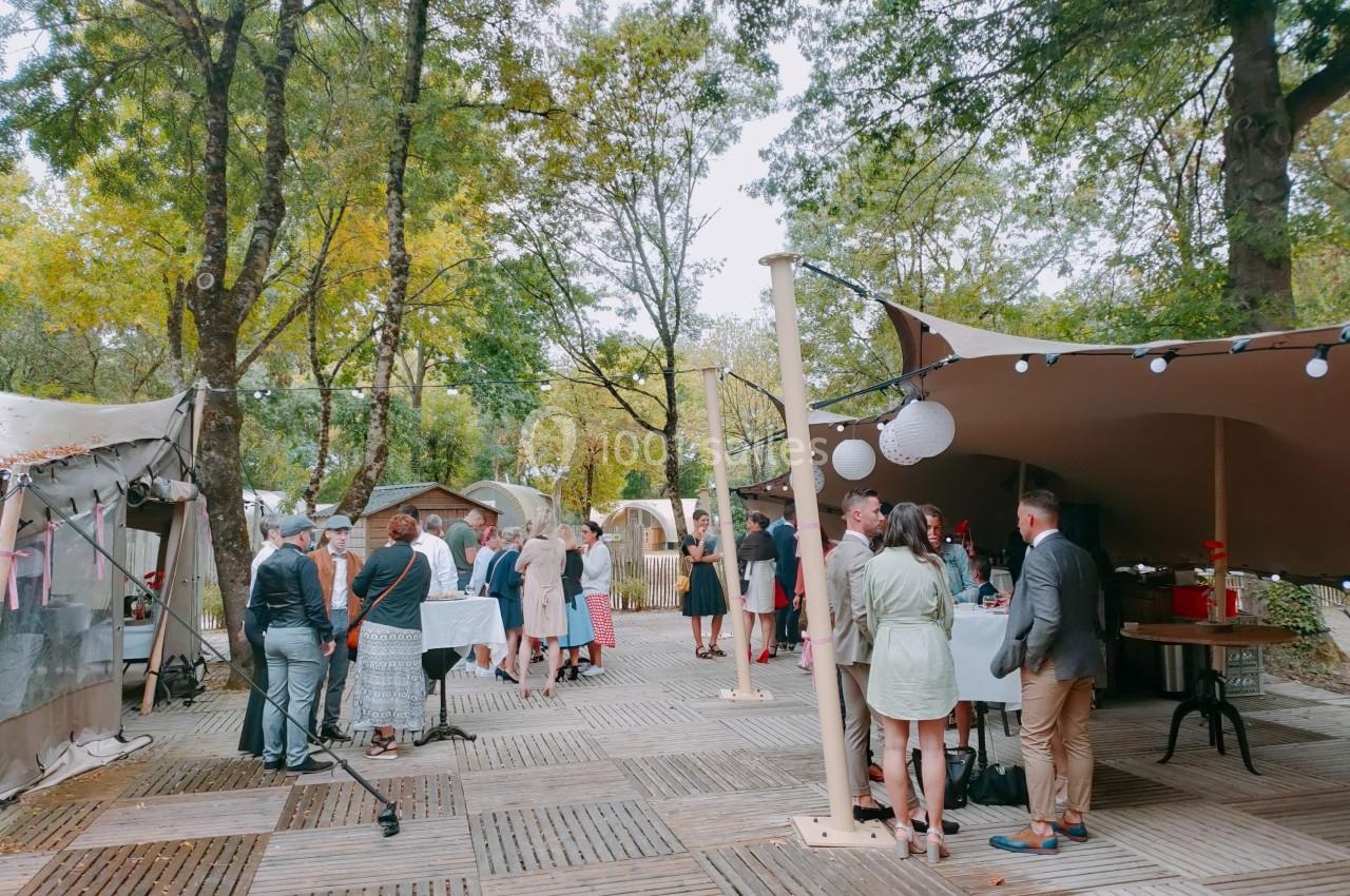 Groupe de personnes rassemblées dans un espace extérieur boisé, sous des tentes, autour de tables hautes.