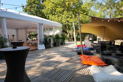 Espace extérieur décoré avec arche florale, deux chaises transparentes et fond blanc sous une tente.