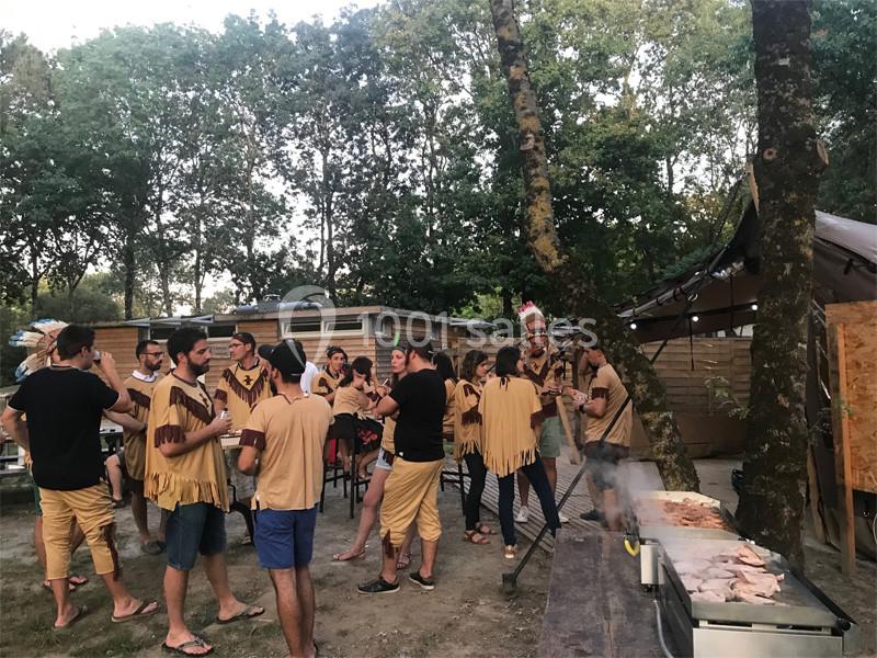 Groupe de personnes en tenue à thème discutant près d'un barbecue dans un espace extérieur boisé.