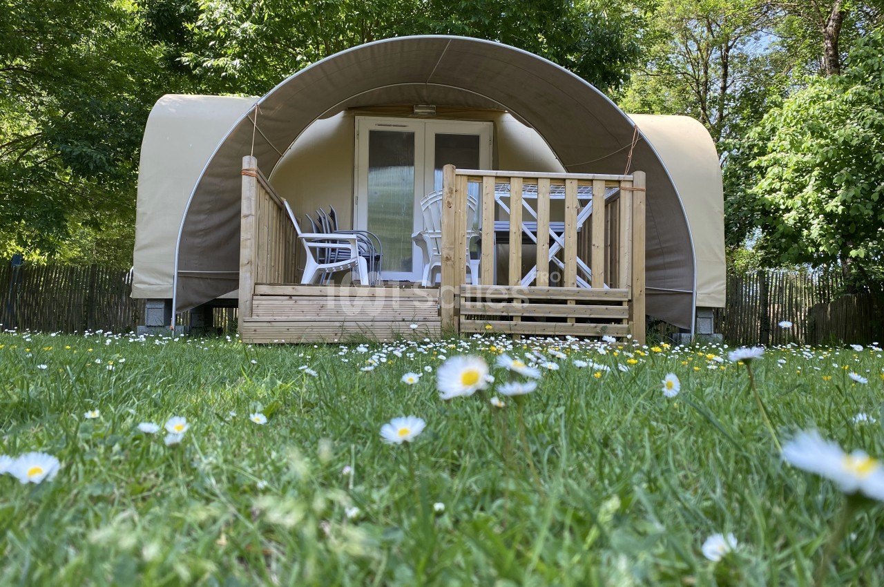 Tente lodge avec terrasse en bois, entourée de pelouse et de marguerites, située dans un environnement arboré.