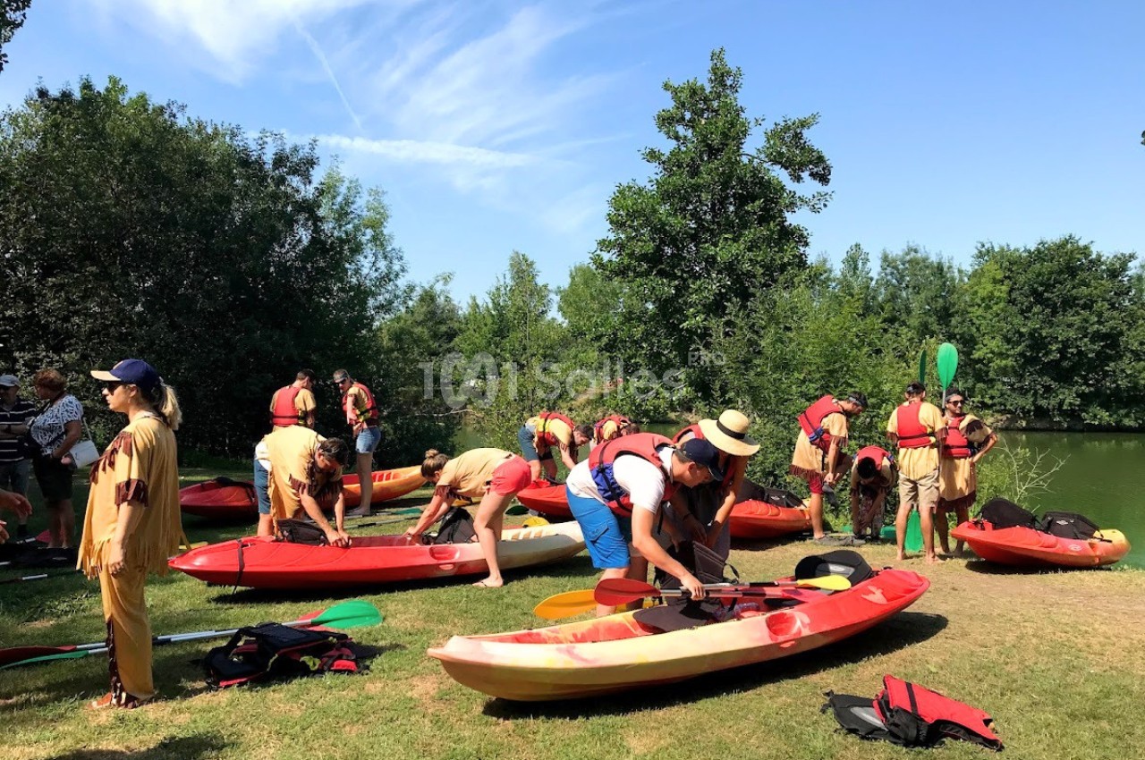 Des personnes en gilets de sauvetage préparent des kayaks sur une pelouse près d'un plan d'eau, par temps ensoleillé.