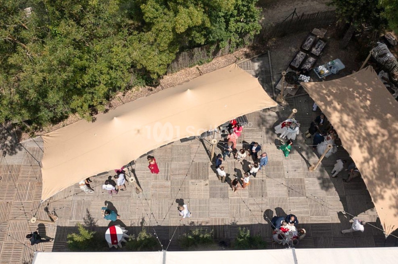Vue aérienne d'un espace extérieur avec des tentes beige, des tables et des personnes réunies sur un sol en bois.
