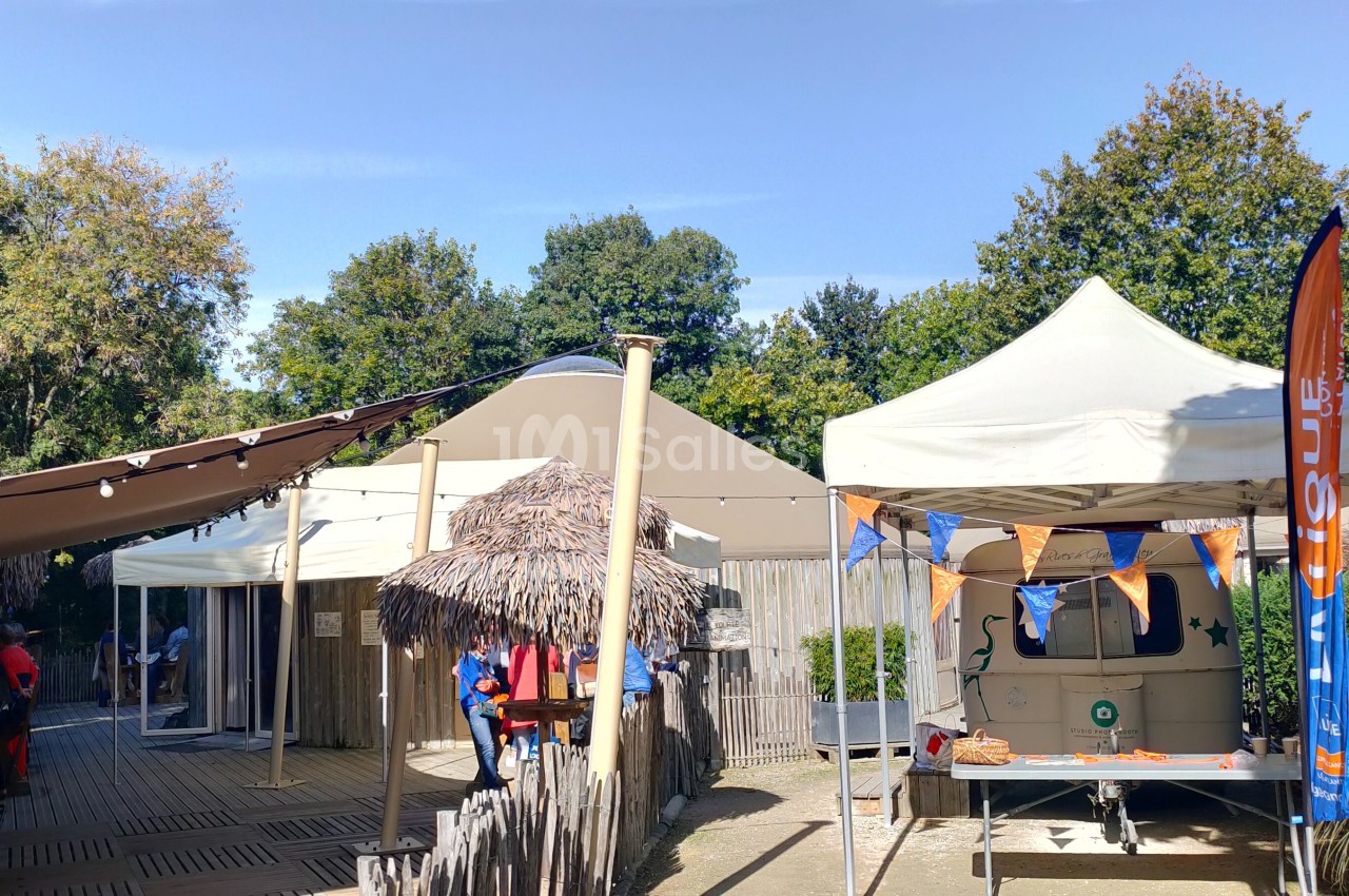 Deux tentes blanches installées dans un espace extérieur arboré, avec des décorations et des structures en bois.