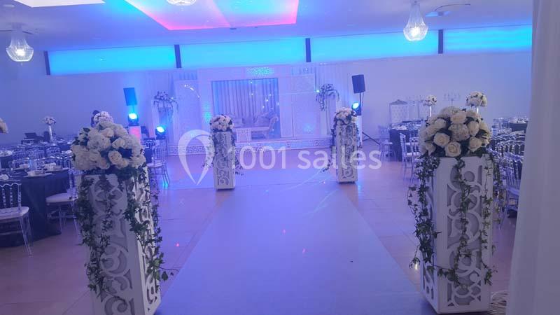 Allée décorée de colonnes fleuries menant à une scène illuminée dans une salle de réception élégante.