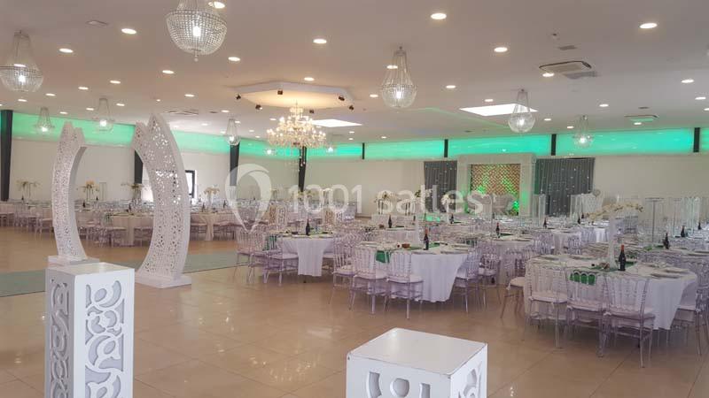Salle de réception décorée avec des tables rondes dressées, des chaises transparentes et un éclairage vert et blanc.