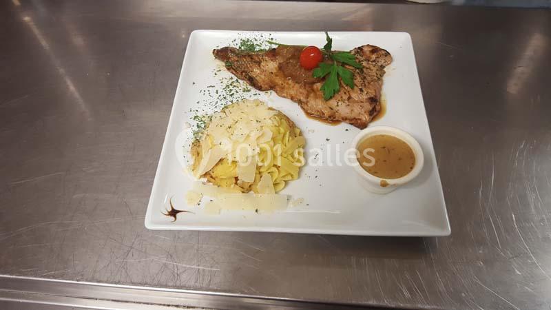 Assiette contenant une escalope grillée garnie de persil et tomate, accompagnée de tagliatelles au parmesan et d'une sauce.